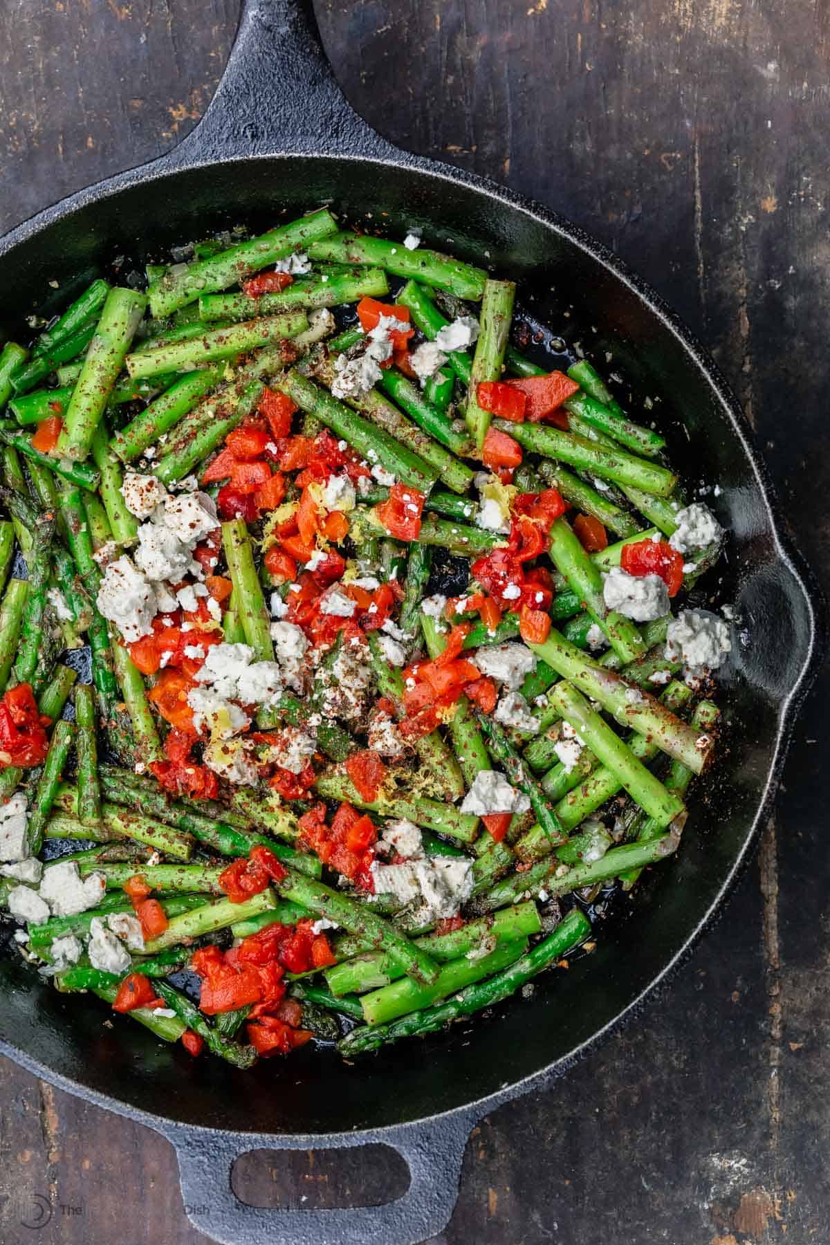 Sauteed asparagus topped with feta and roasted red peppers in a cast iron skillet