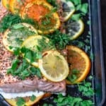 Citrus salmon on a baking sheet topped with lemon and orange slices, dried mint and oregano