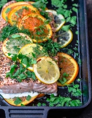 Citrus salmon on a baking sheet topped with lemon and orange slices, dried mint and oregano