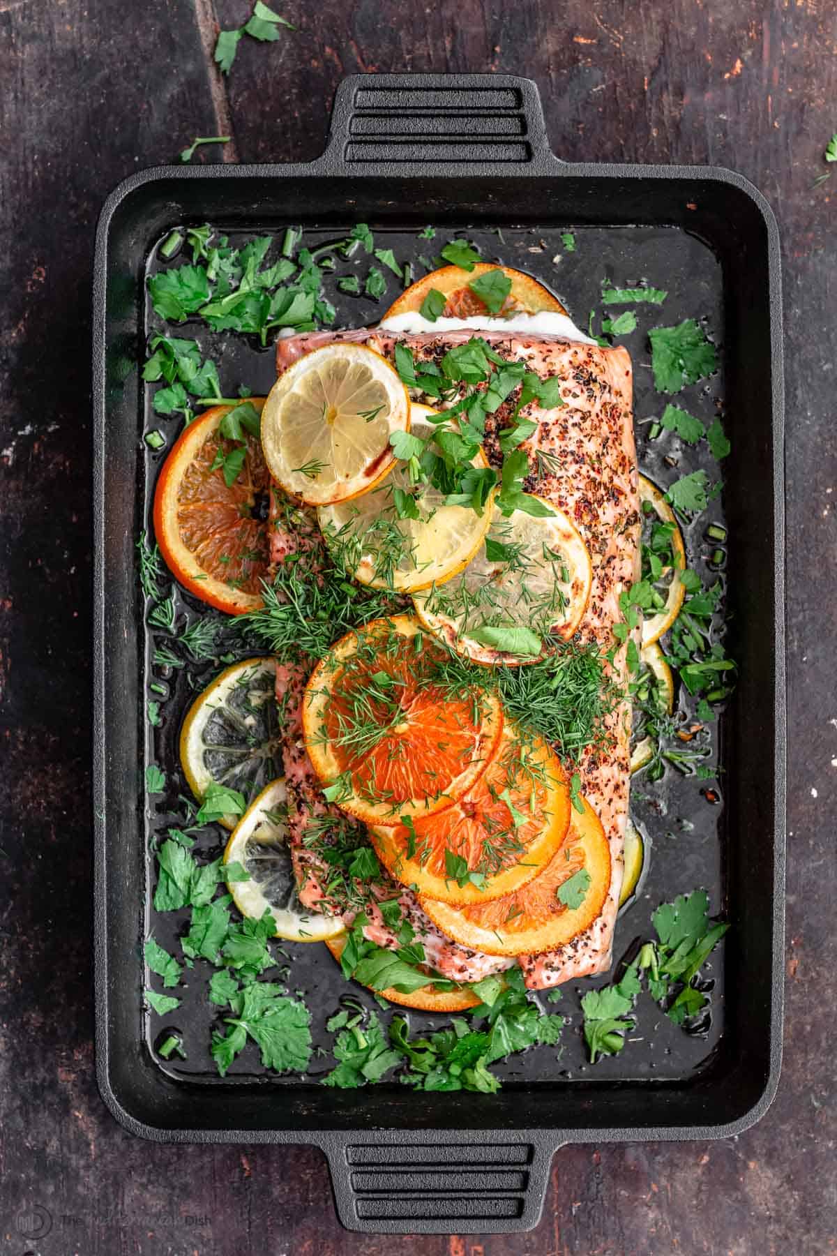 Fillet of salmon in skillet with slices of oranges and lemons