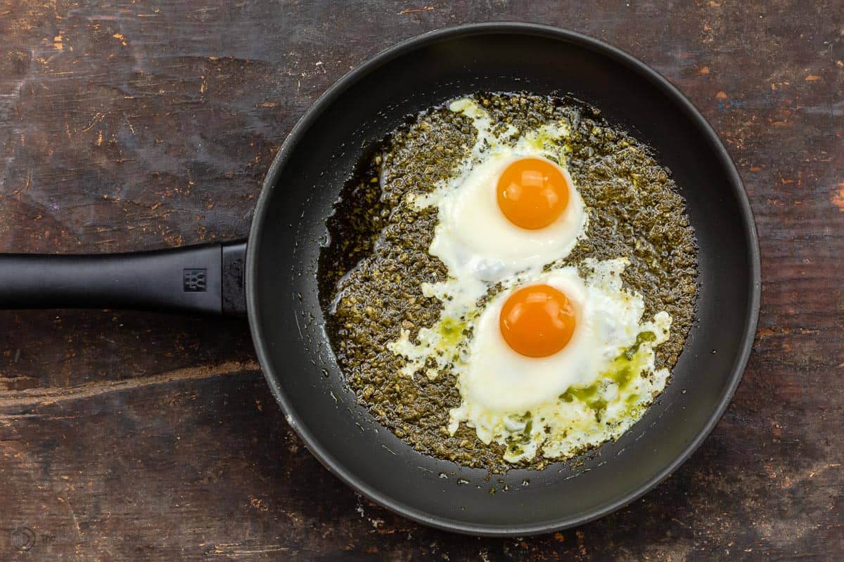 Two sunny side eggs in frying pan with pesto sauce