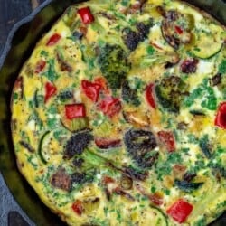 A Vegetable Frittata in a Round, Black Pan on Top of a Wooden Table