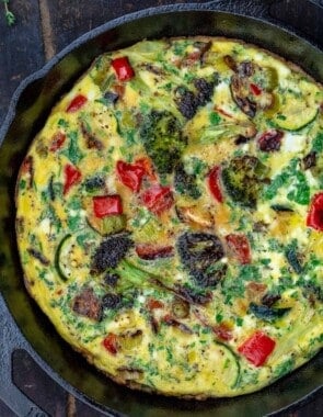 A Vegetable Frittata in a Round, Black Pan on Top of a Wooden Table