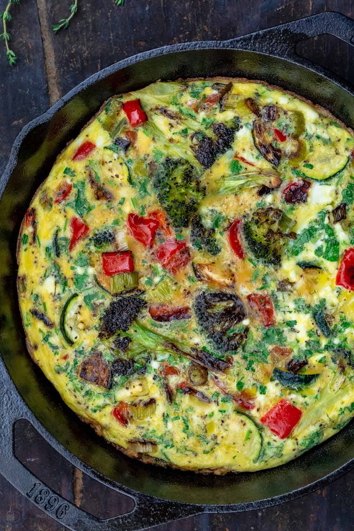 A Vegetable Frittata in a Round, Black Pan on Top of a Wooden Table