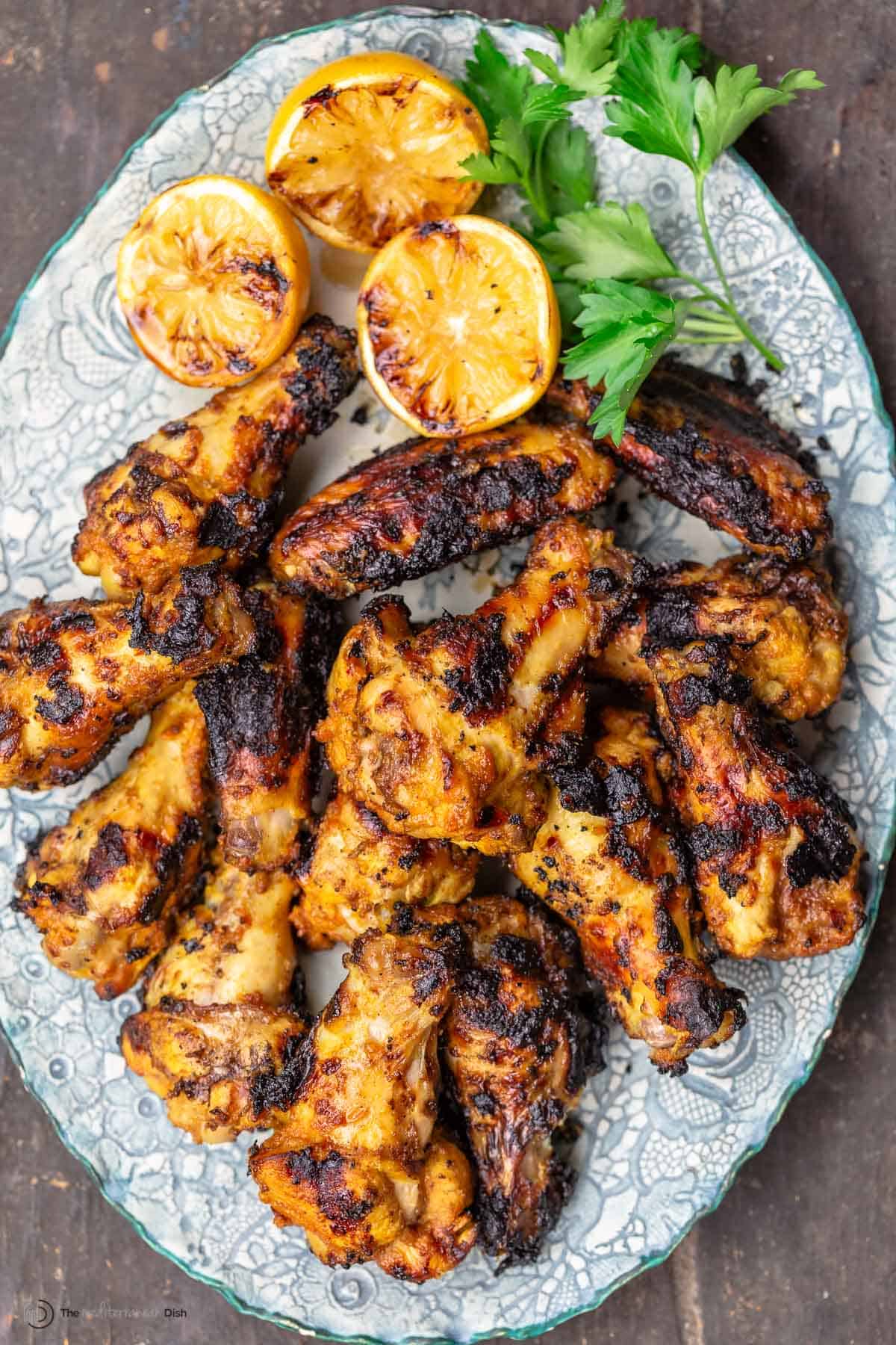 Overhead view of chicken wings that have been grilled, on a plate with lemons