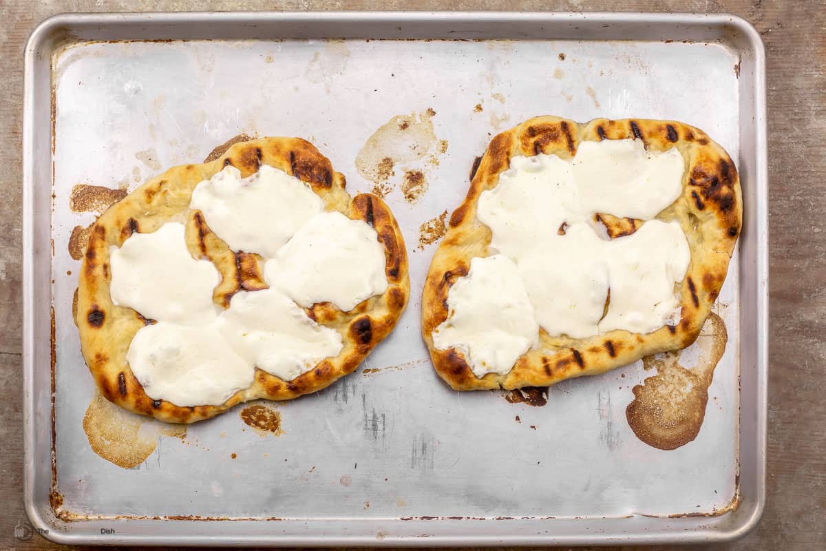 Two pizza crusts on a baking sheet, topped with melted mozzarella