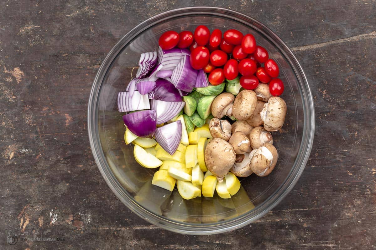 Grape tomatoes, red onion, baby bella mushrooms, squash and brussels sprouts in a mixing bowl