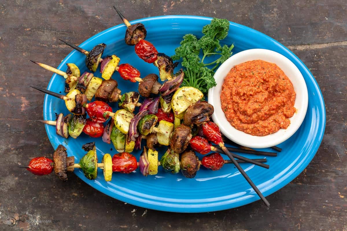 Grilled veggie skewers on a plate with romesco sauce