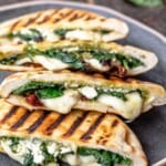 pita grilled cheese sandwiches with melted mozzarella, feta, spinach and sundried tomatoes on a platter