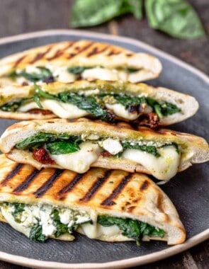 pita grilled cheese sandwiches with melted mozzarella, feta, spinach and sundried tomatoes on a platter