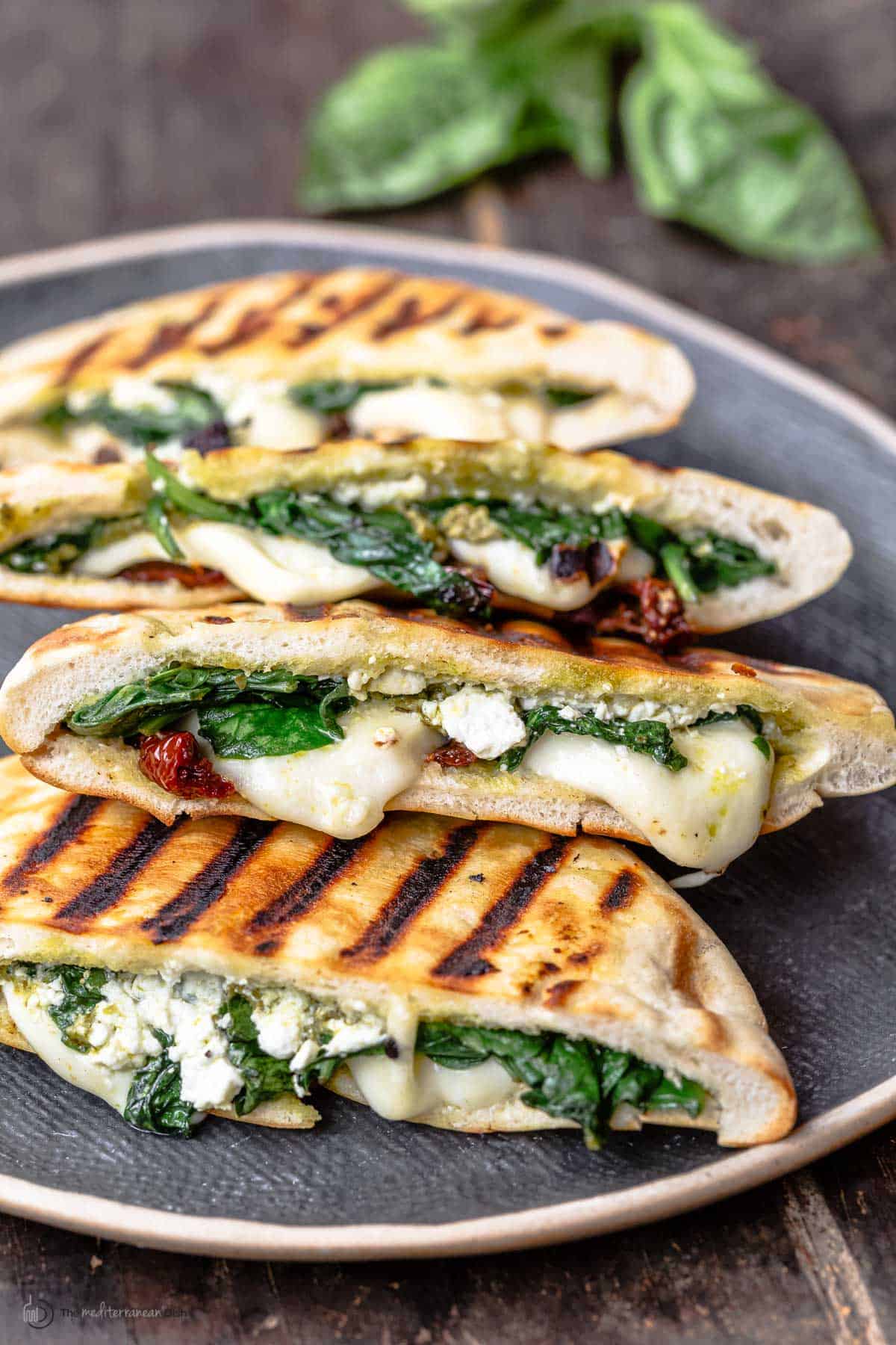 pita grilled cheese sandwiches with melted mozzarella, feta, spinach and sundried tomatoes on a platter