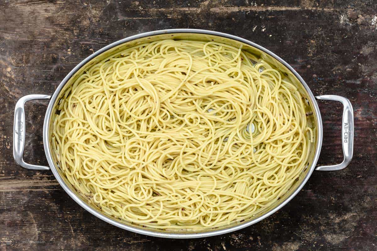 A large pan with spaghetti added to olive oil garlic and pasta water