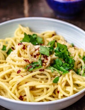 A bowl of olive oil and garlic pasta topped with parsley, red pepper flakes and parmesan