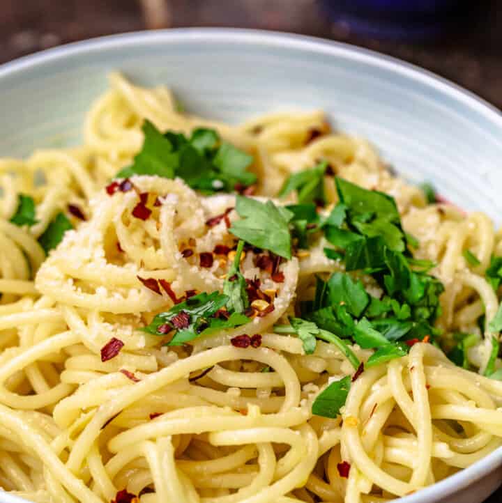 A bowl of olive oil and garlic pasta topped with parsley, red pepper flakes and parmesan