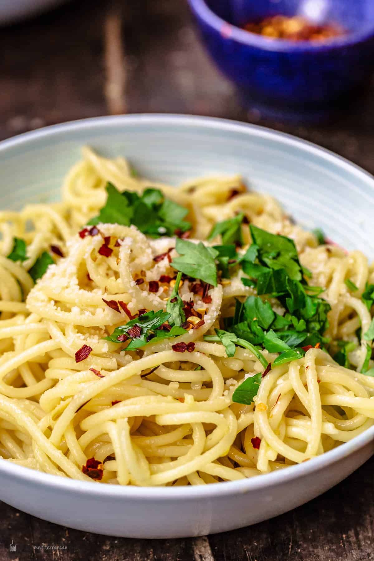 A bowl of olive oil and garlic pasta topped with parsley, red pepper flakes and parmesan