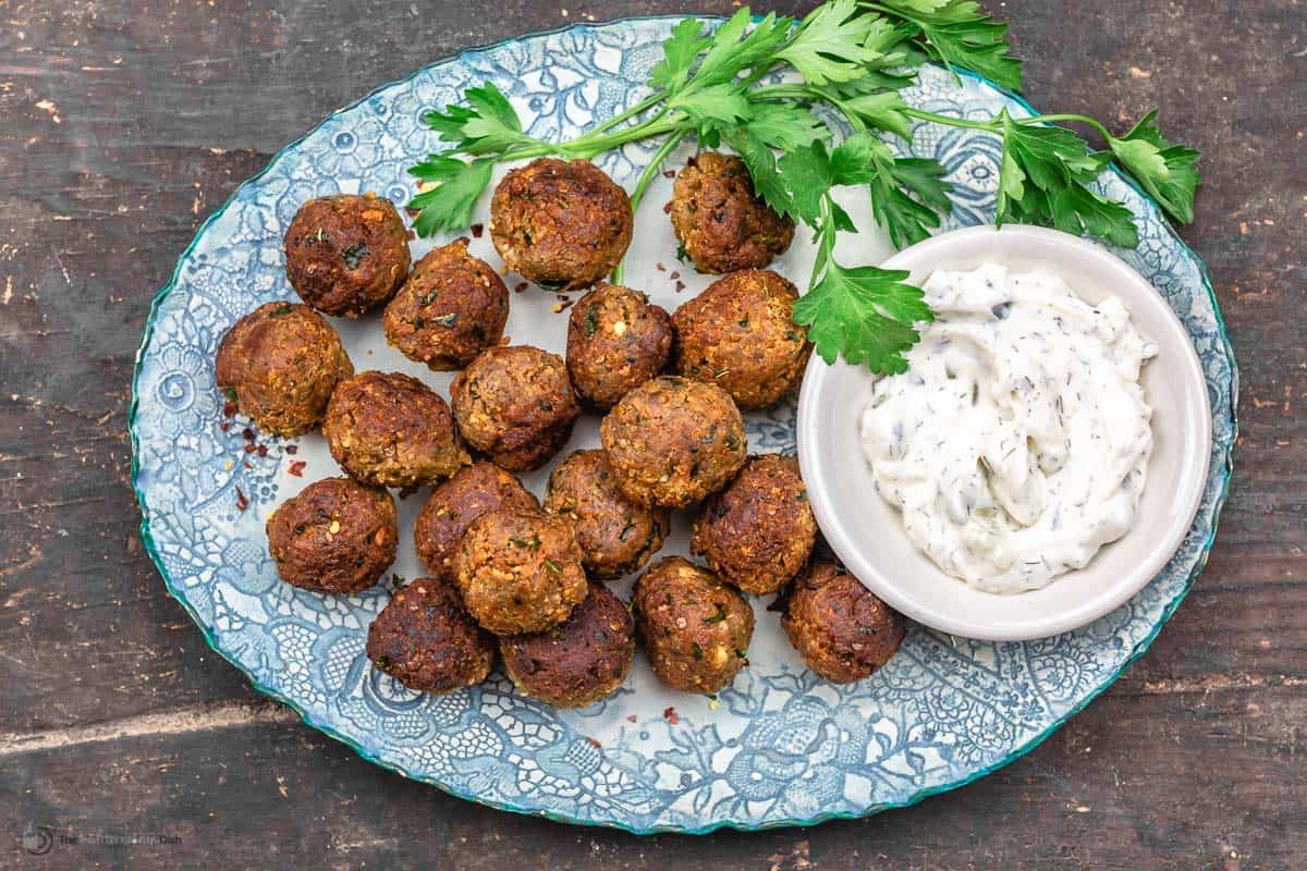 Vegan meatballs with eggplant on a blue plate, next to a dish of tzatziki