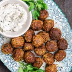 Vegan meatballs with eggplant on a blue plate, next to a dish of tzatziki