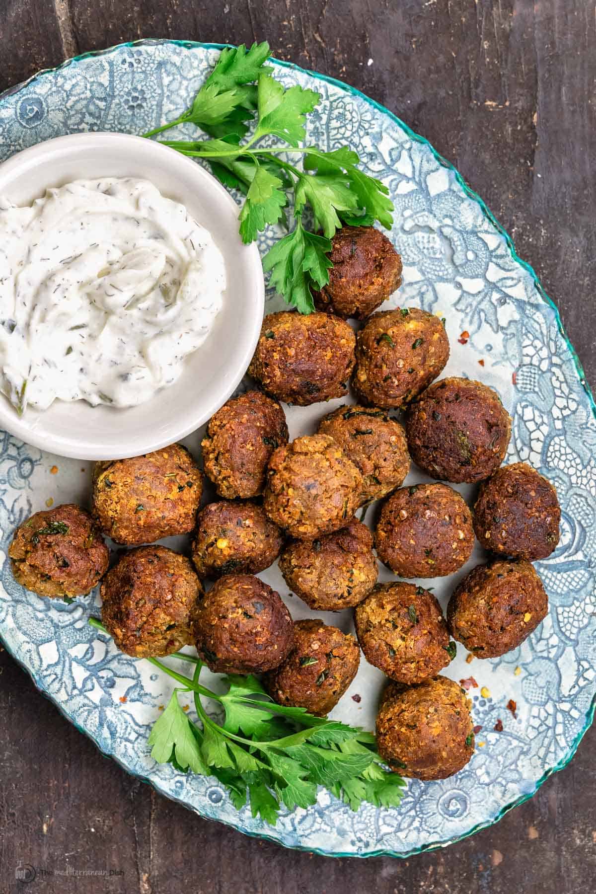 Vegan meatballs with eggplant on a blue plate, next to a dish of tzatziki