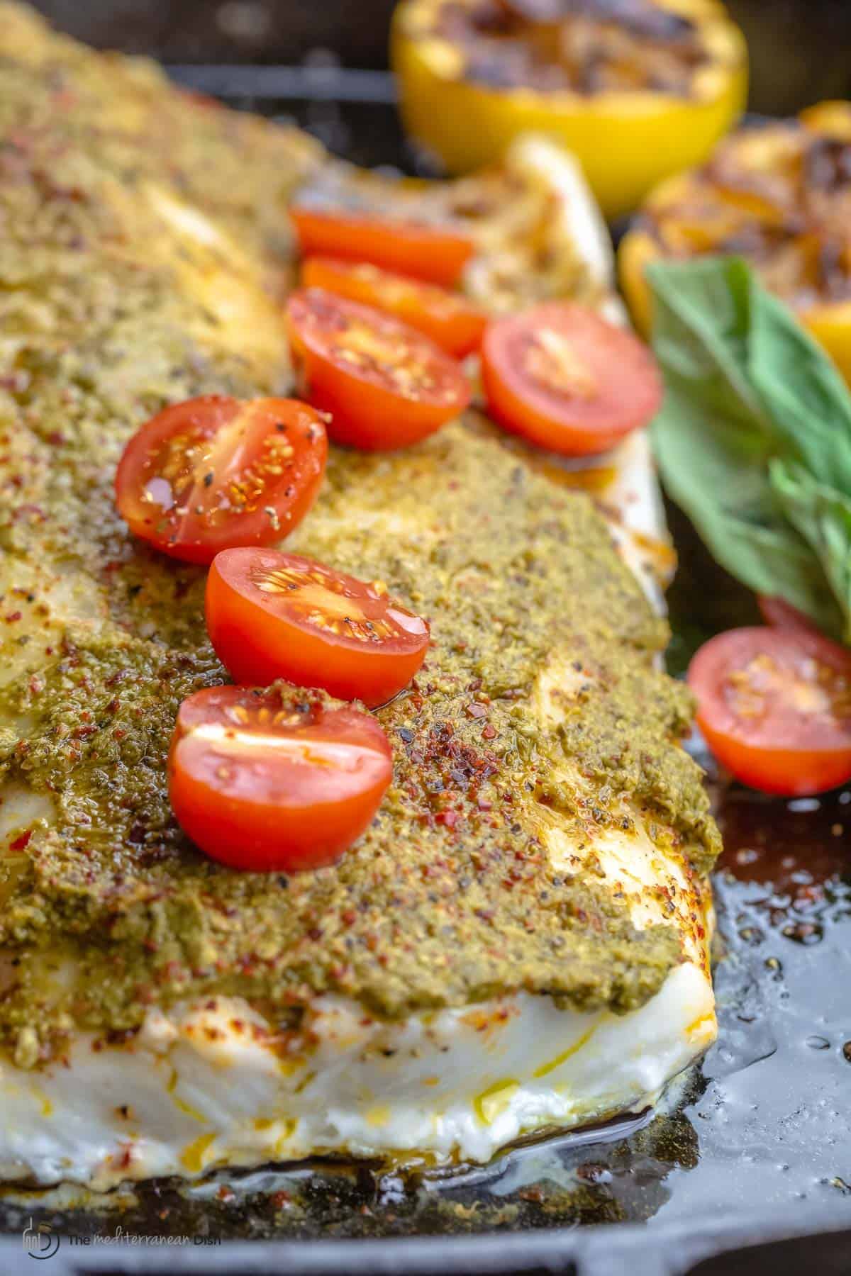 Close-up of a baked sea bass fillet with basil pesto and grape tomato halves