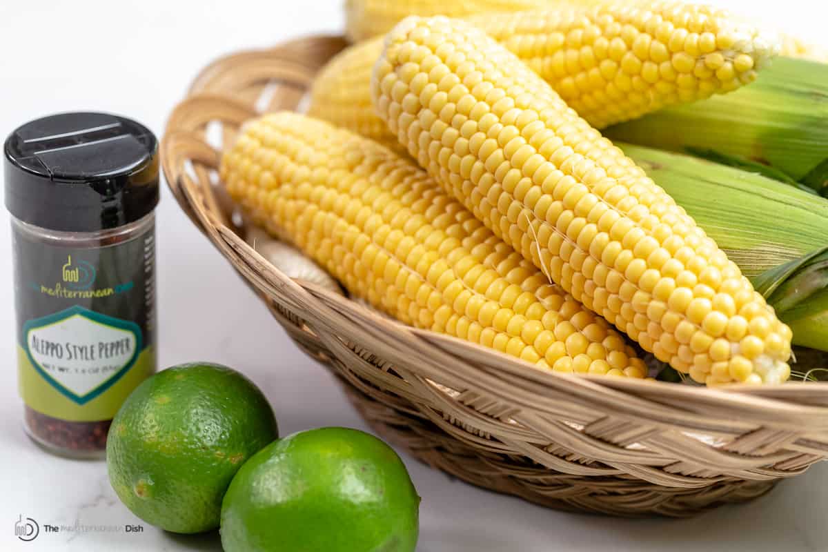 A bowl of corn ears with limes and Aleppo pepper in front