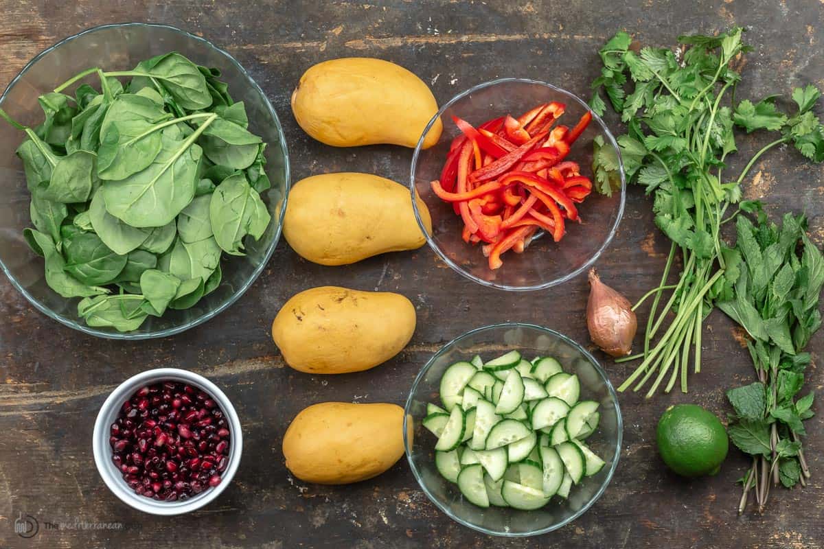 Overhead view of mango salad ingredients - spinach, pomegranate seeds, mangos, cucumbers, peppers, shallots, lime