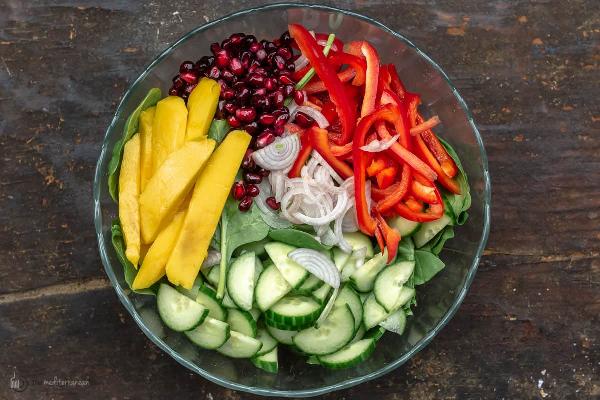 All of the ingredients to make mango spinach salad in a glass bowl