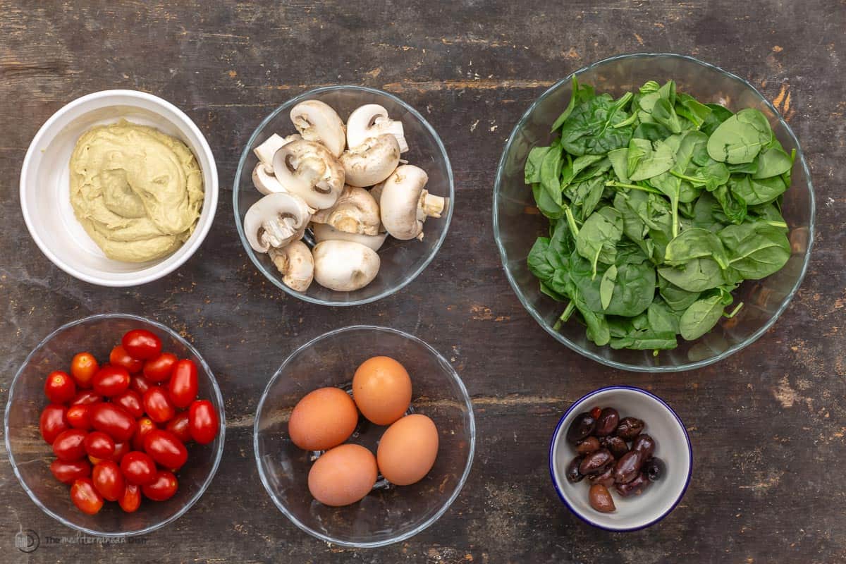 Hummus, mushrooms, spinach, tomatoes, eggs and seasonings all in individual bowls