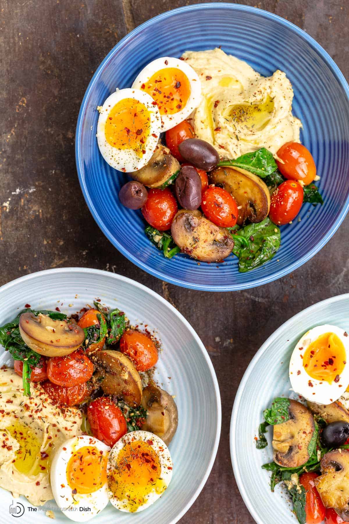 Two savory breakfast bowls with eggs, vegetables and hummus