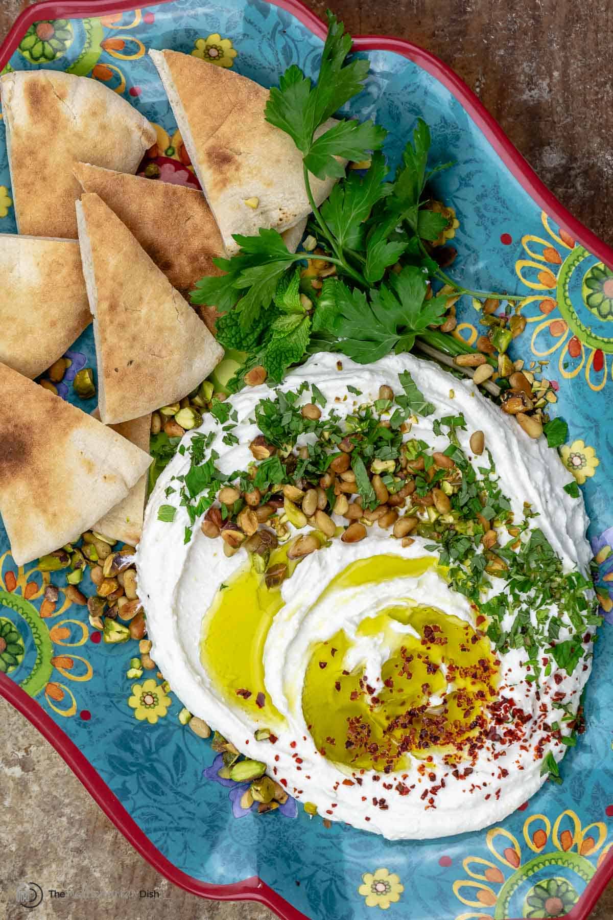 Whipped feta cheese topped with olive oil and fresh herbs on a tray with pita chips