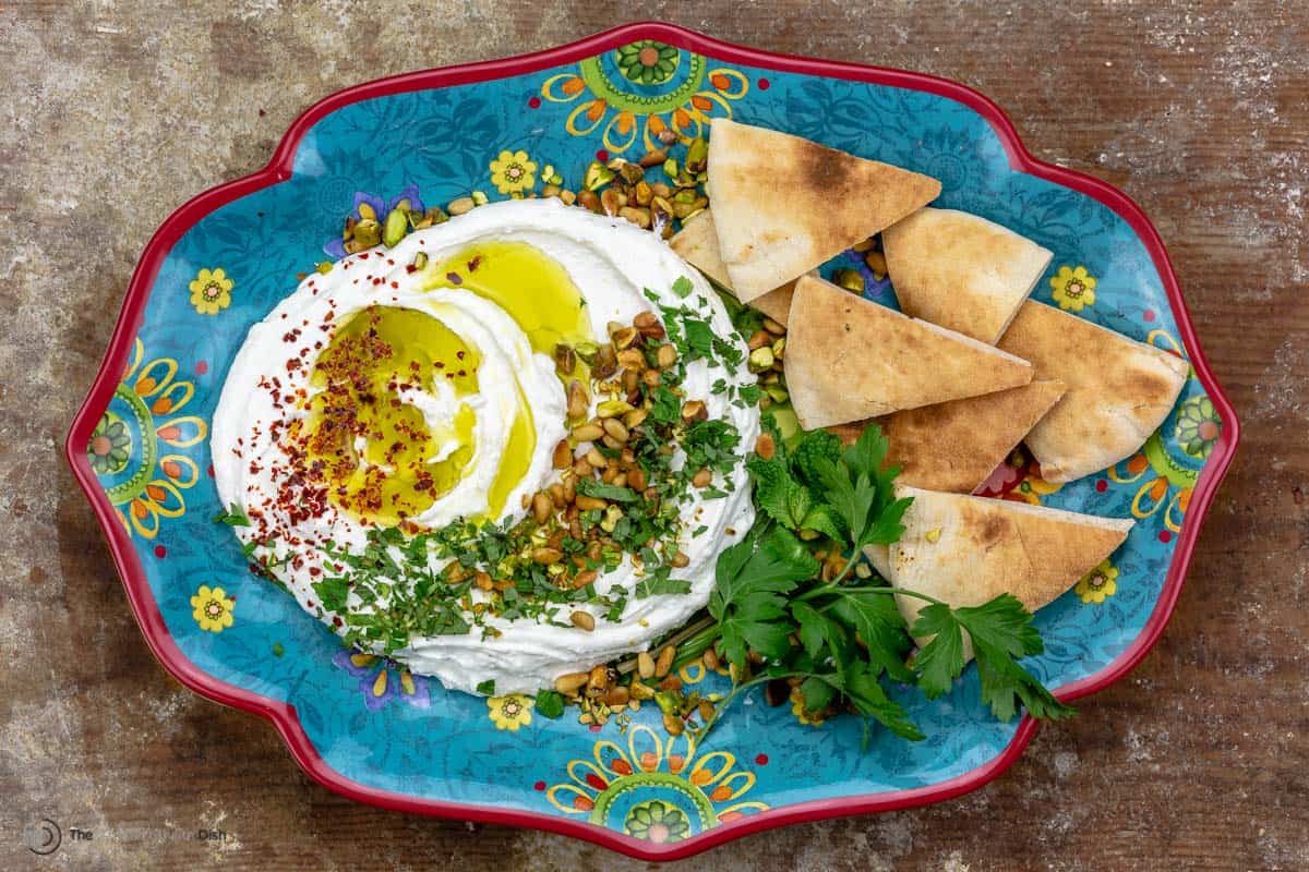 Whipped feta dip topped with olive oil and herbs, served with pita chips, on a blue plate