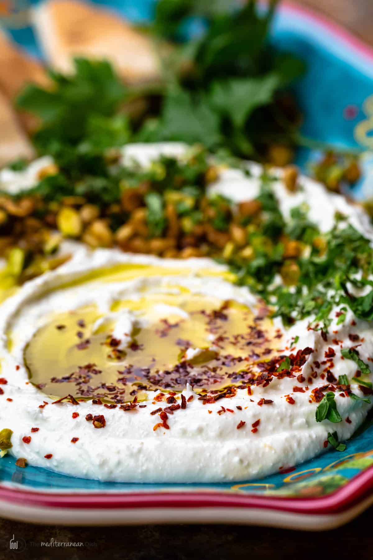 Whipped feta dip on a plate with olive oil, Aleppo pepper and fresh herbs