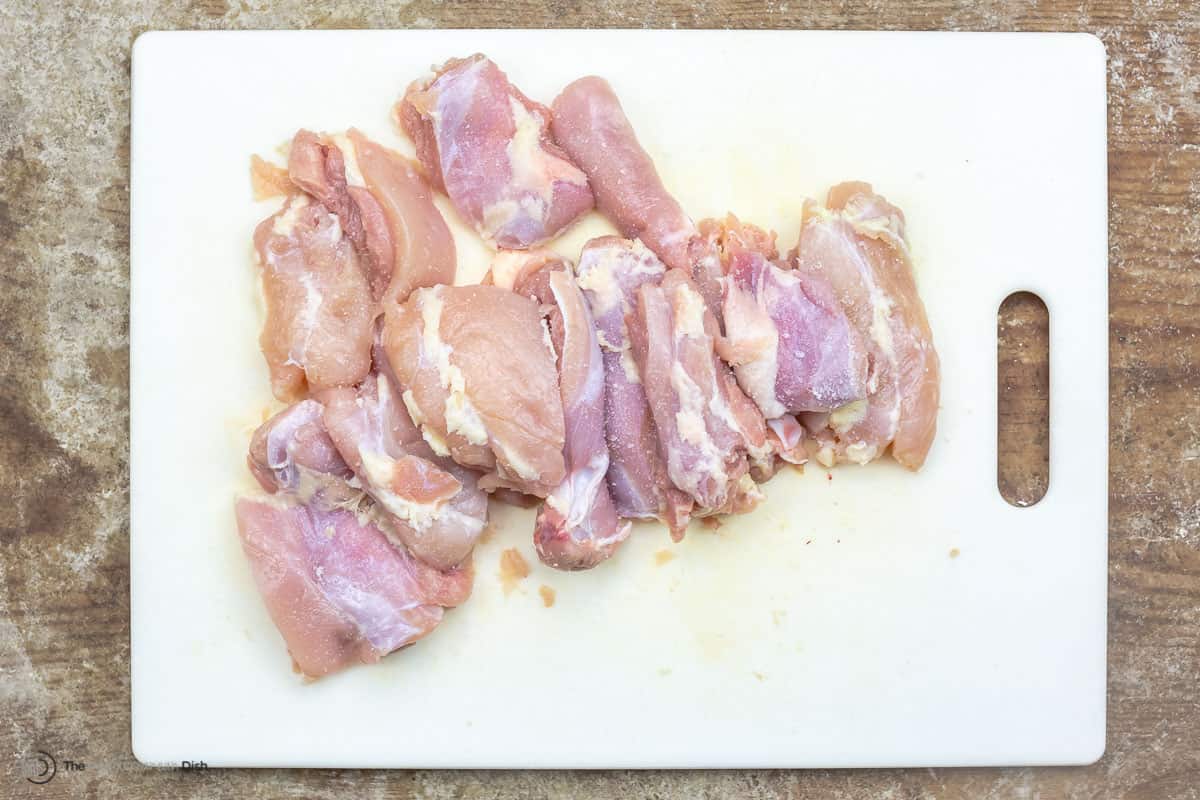 Boneless skinless chicken thighs cut into pieces on a cutting board