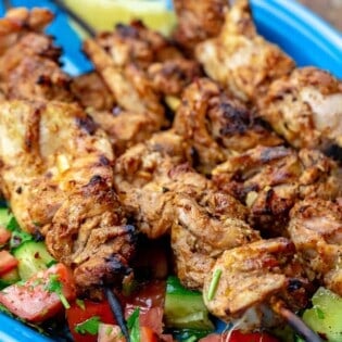 Chicken tawook grilled chicken skewers on a blue plate with salad