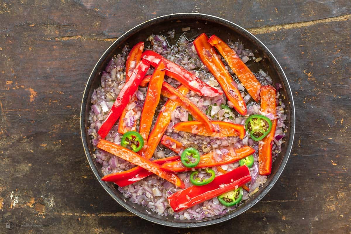 A large skillet with chopped onions, red peppers, jalapenos and garlic