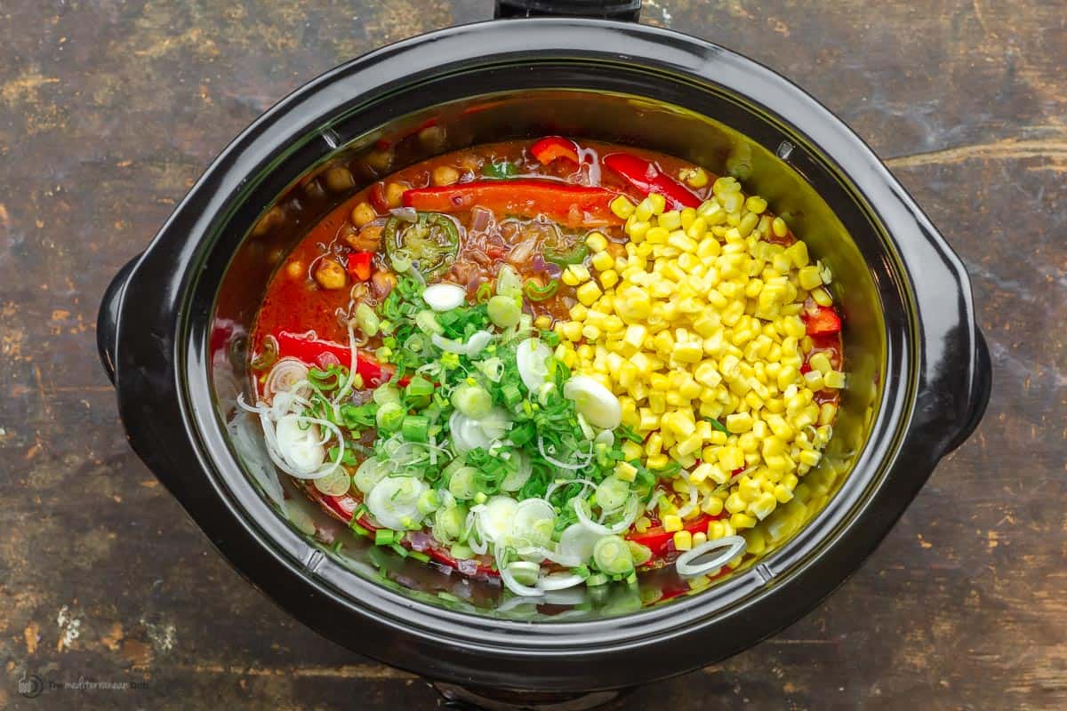 Scallions and corn being added to slow cooker chili