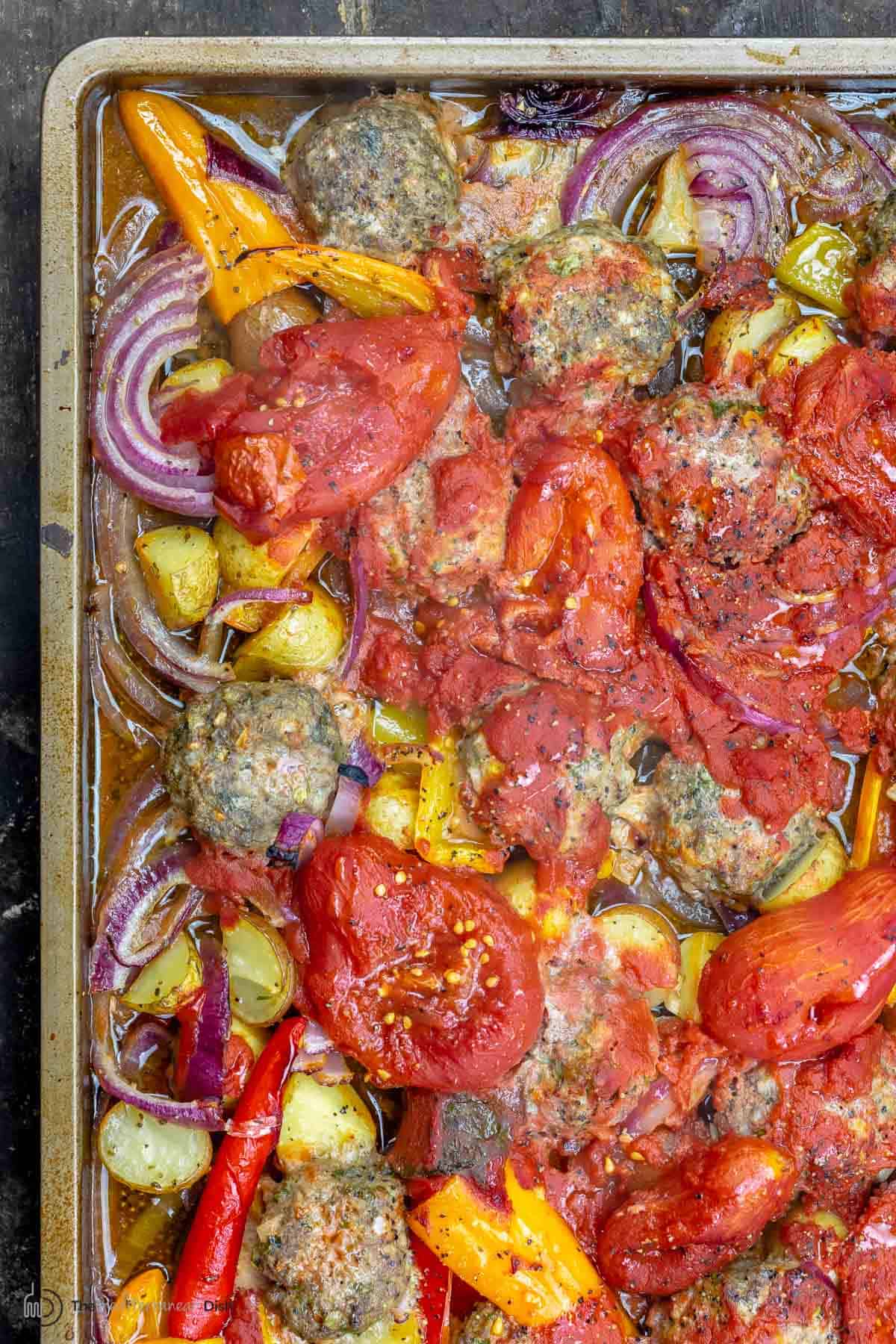 Close-up of baked meatballs with tomatoes and other vegetables in a sheet pan