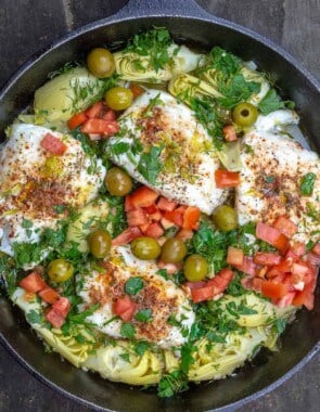 Overhead view of lemon haddock fillets with artichoke hearts and tomatoes in a skillet