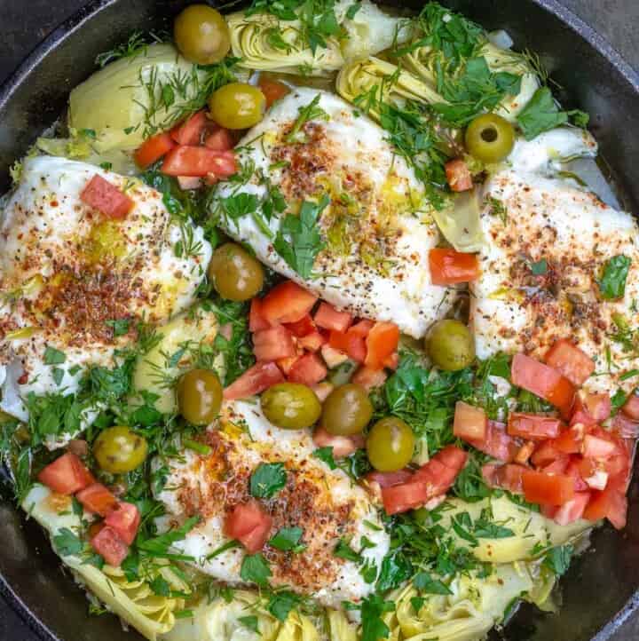 Overhead view of lemon haddock fillets with artichoke hearts and tomatoes in a skillet