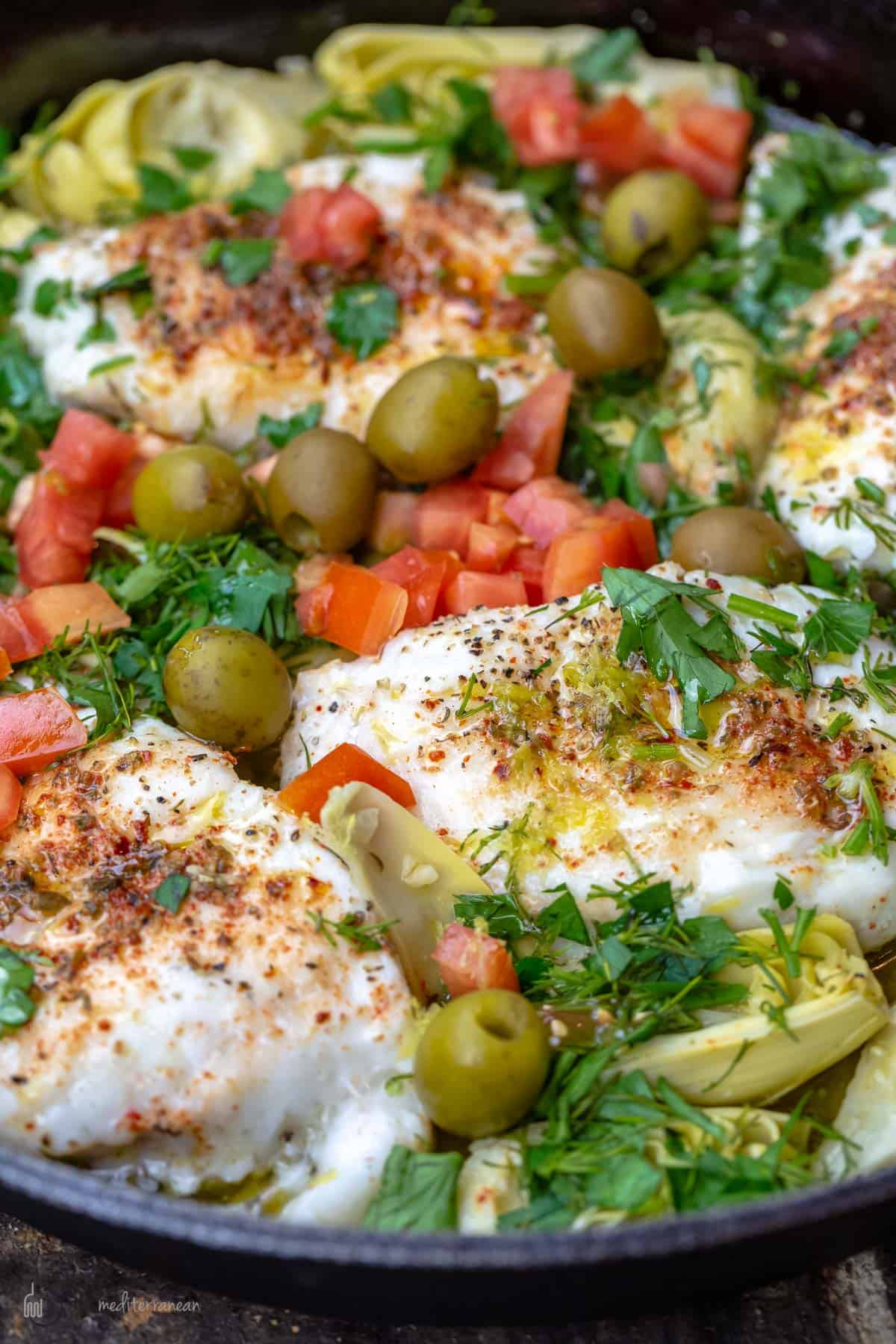 Lemon haddock fillets with fresh herbs artichoke hearts and tomatoes in a skillet