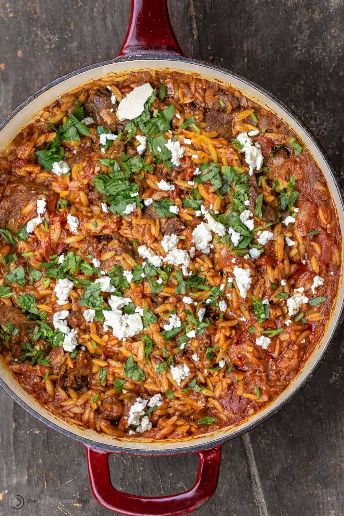 Overhead view of youvetsi garnished with feta and parsley in a large pan