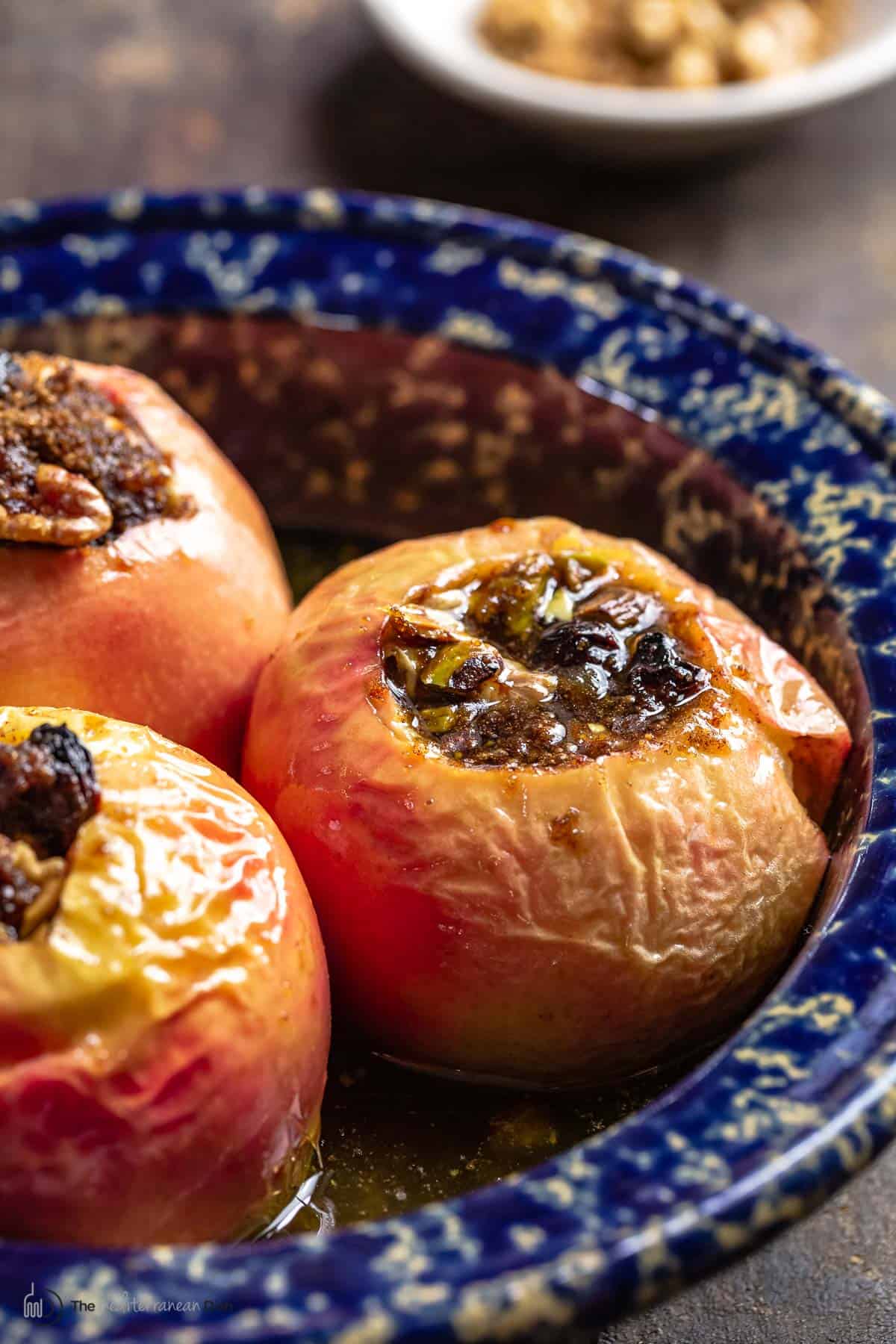 Baked apples in their blue baking dish with another small dish of extra nuts to the side