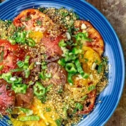 Heirloom tomato salad on a blue plate, topped with dukkah and jalapeno peppers