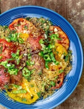 Heirloom tomato salad on a blue plate, topped with dukkah and jalapeno peppers