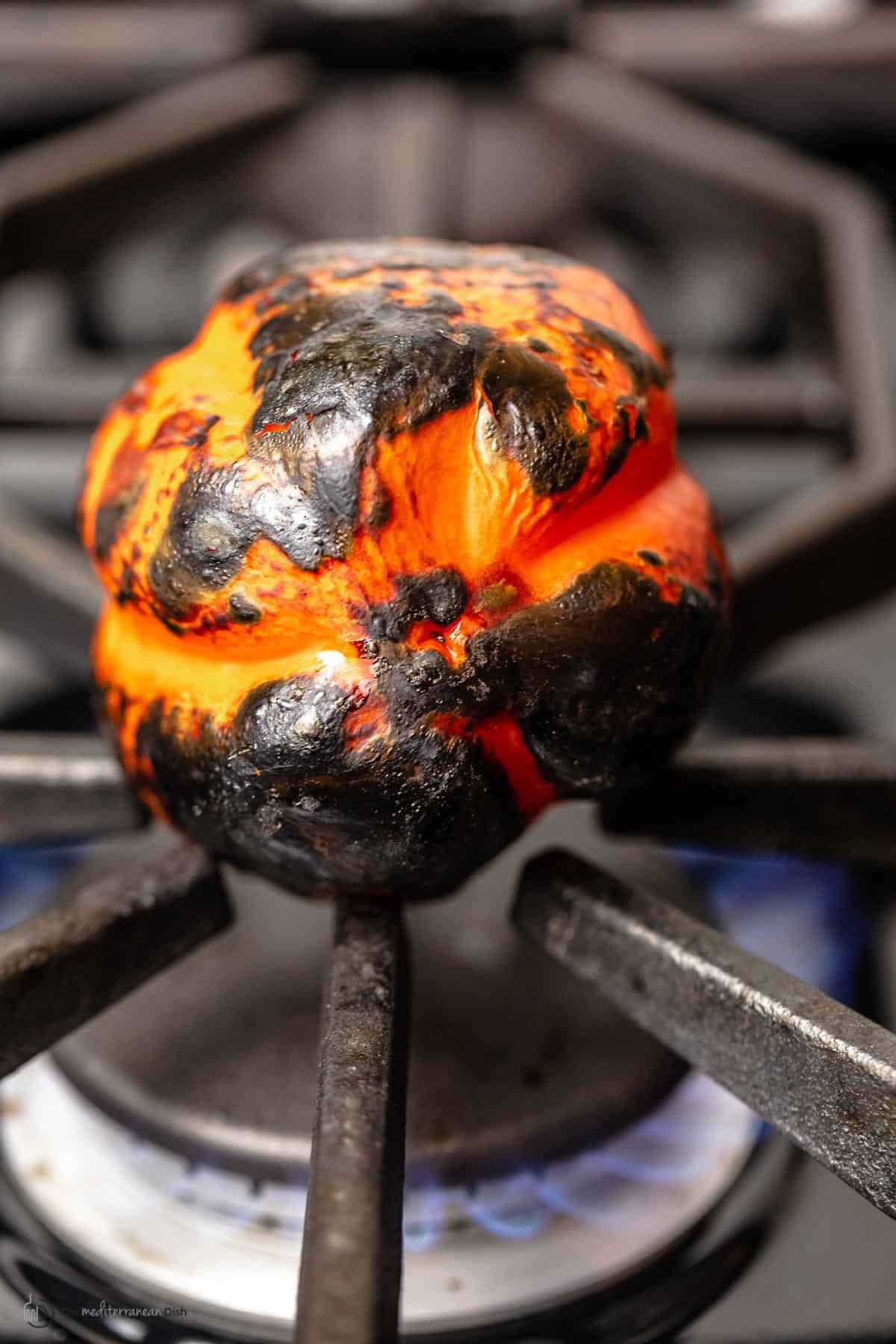 An orange bell pepper roasting on the stovetop