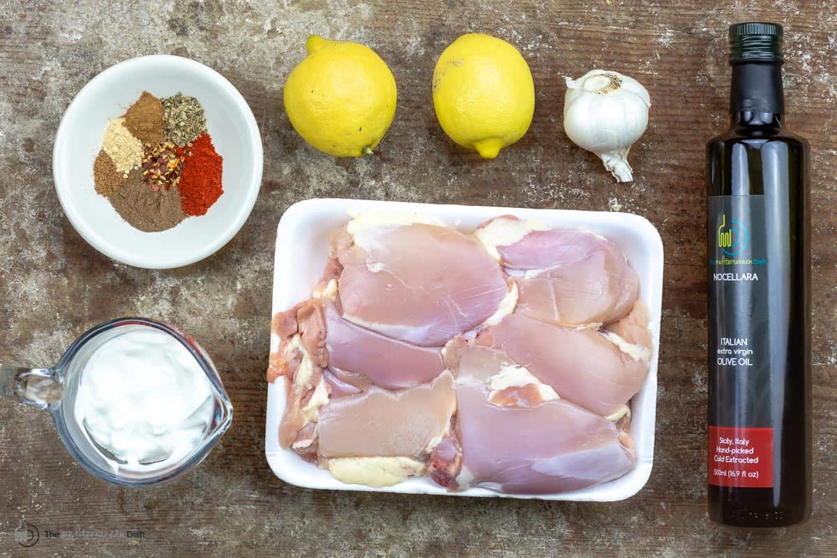 ingredients for making shish tawook, including boneless chicken, garlic spices, yogurt, olive oil, and lemons