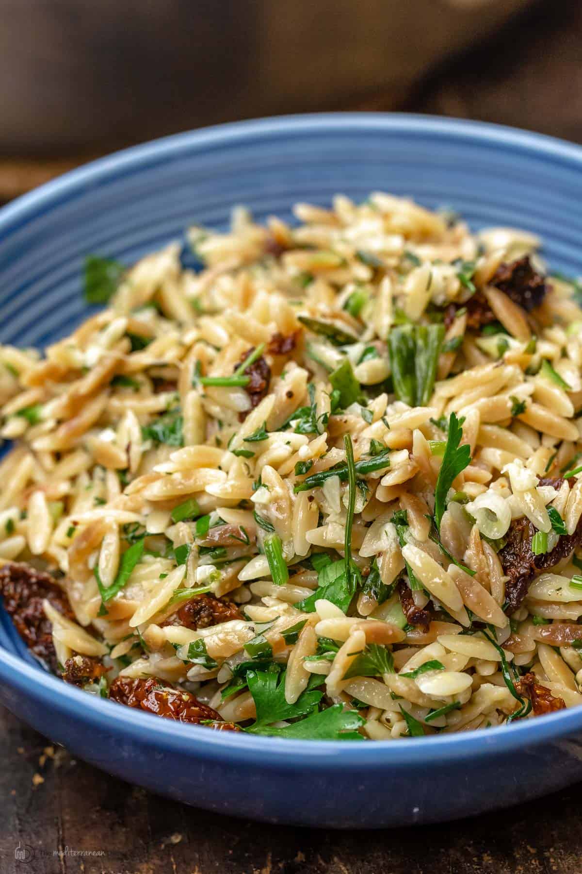 toasted orzo recipe served in blue bowl with sundried tomatoes and a garnish of parsley