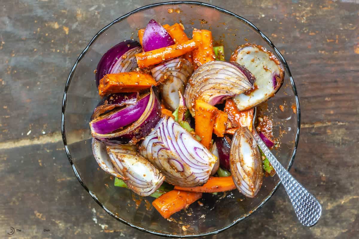 Onions, celery and carrots coated in marinade in a glass bowl