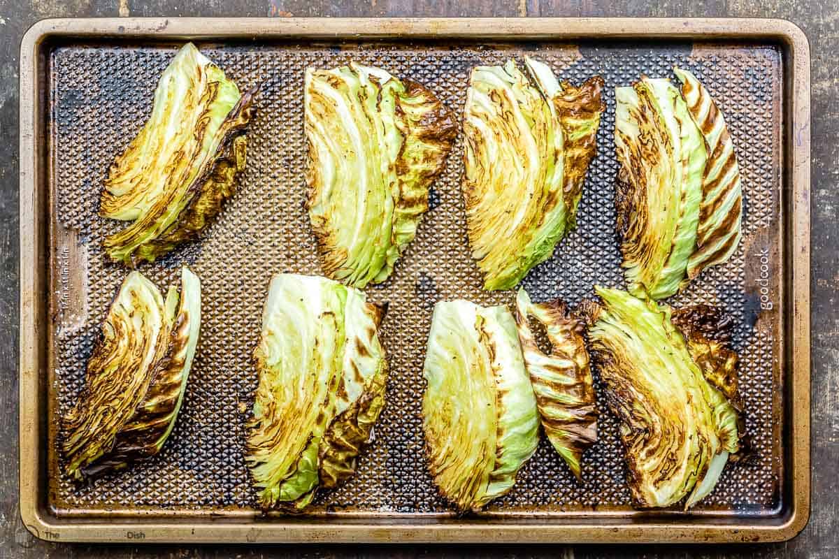 Eight roasted cabbage wedges on a baking sheet