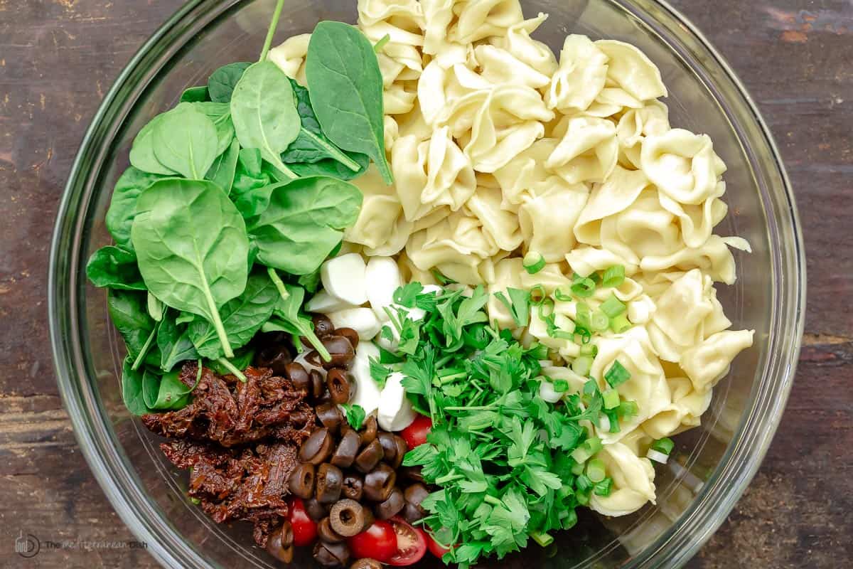 Overhead view of tortellini salad ingredients in a glass bowl