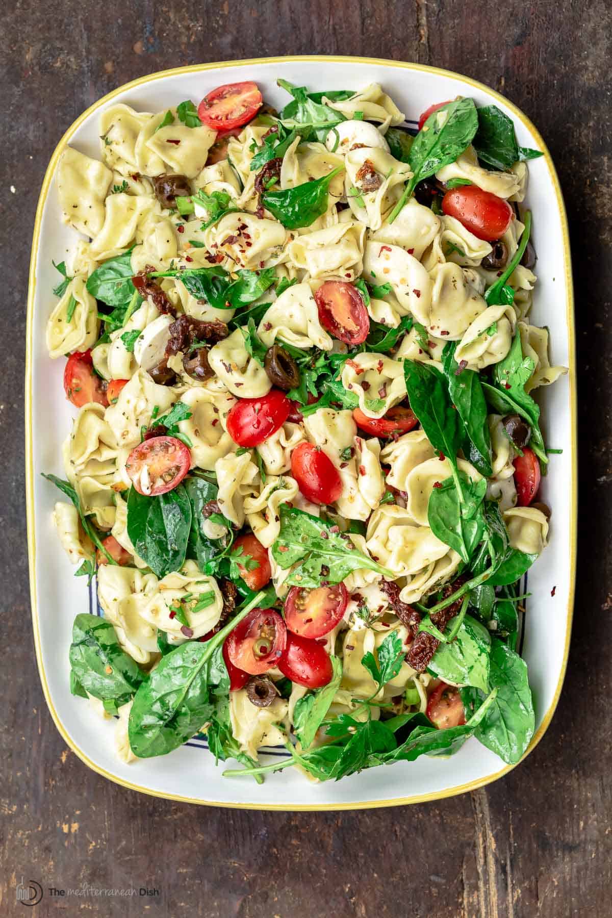 Overhead view of Mediterranean tortellini salad with spinach on a white serving platter